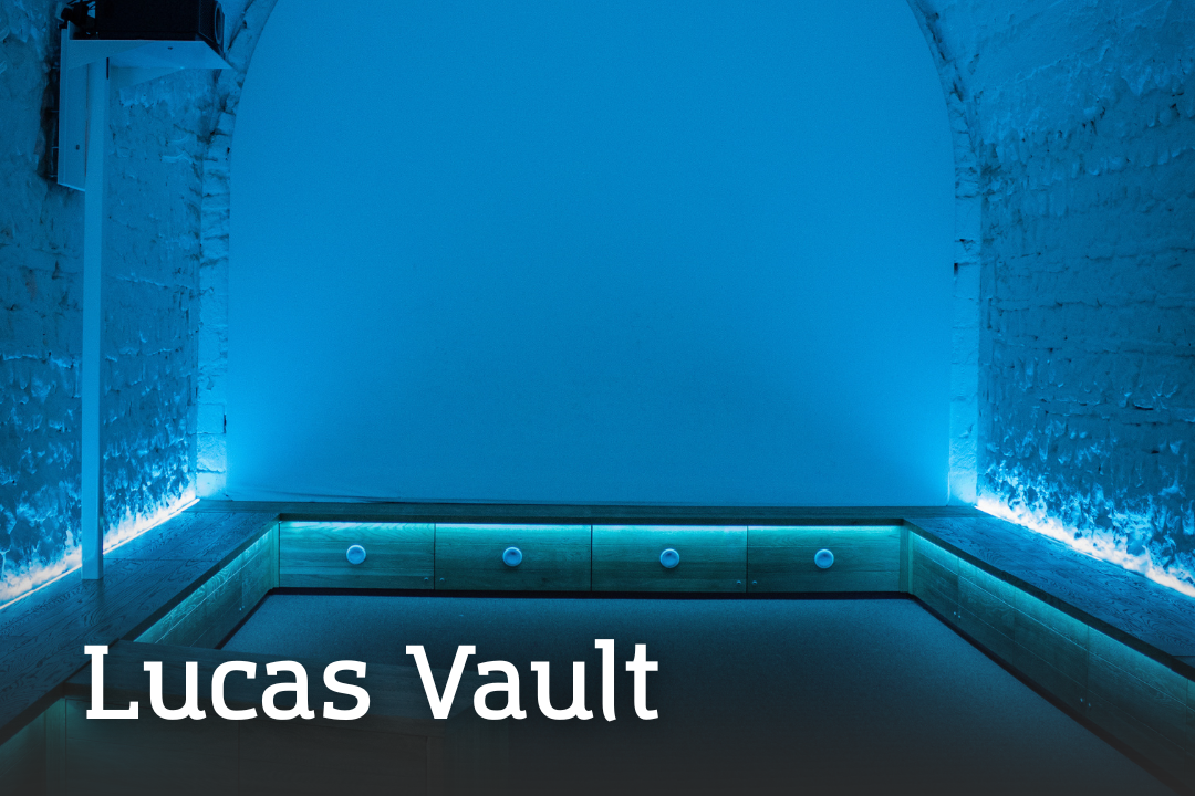 Lucas Vault Lucas Vault A vaulted chamber lit with cool blue lighting, featuring a recessed central area bordered by low wooden panels with built‑in lights.