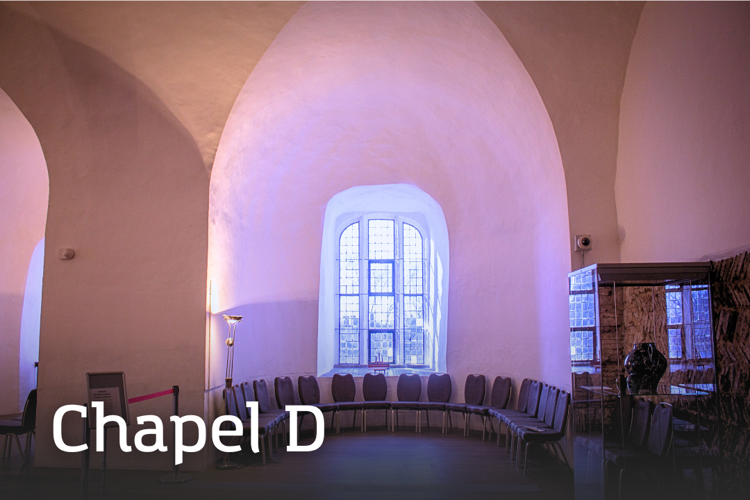 Chapel D Chapel D A large chapel space with high vaulted ceilings and pale walls. A long row of padded chairs lines the curved wall beneath a tall arched window.