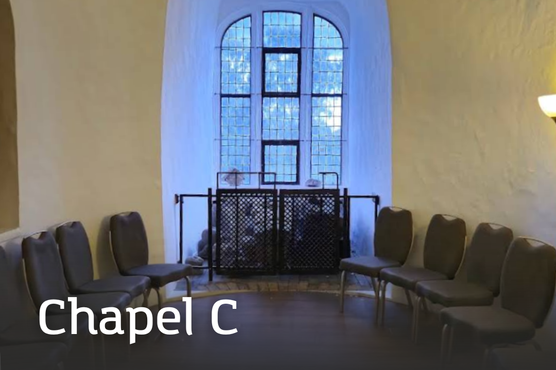 Chapel C Chapel C A small curved chapel space with pale stone walls, arched ceilings, and a large leaded window. A semicircle of padded chairs is arranged around the room.
